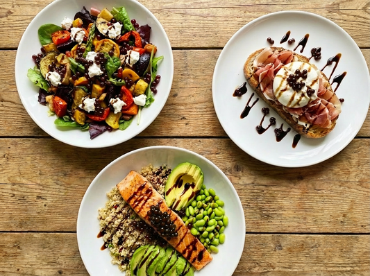 Three gourmet dishes on white plates are arranged on a rustic wooden table. Each dish is topped with glossy, dark balsamic pearls that look natural and appetising. 