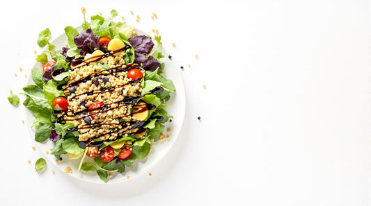 Fresh leaf and grain salad drizzled with simply balsamic dressing on a white background, featuring quinoa and mixed greens in a minimalist presentation