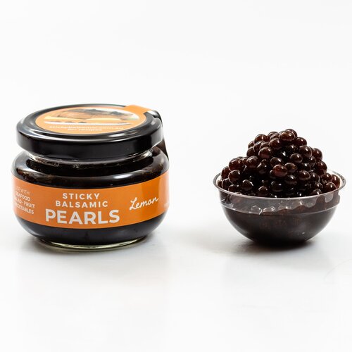 Sticky Balsamic Lemon Pearls jar next to some lemon pearls in a plastic container, with a white background.