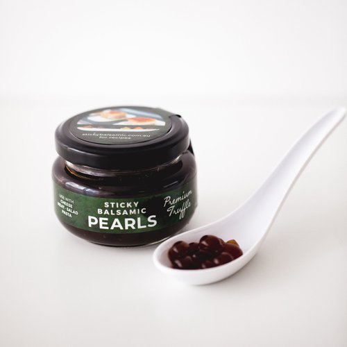 Sticky Balsamic Premium Truffle Pearls Jar next to a spoon with several pearls in it, with a white background