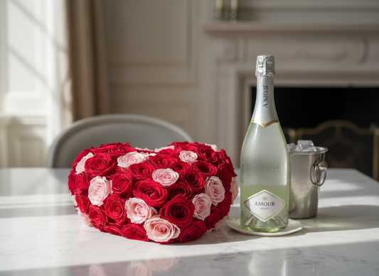 Heart-shaped arrangement of fresh red and pink roses with a chilled bottle of sparkling wine on a white marble table, beautifully lit for a romantic and elegant Valentine’s Day setting.