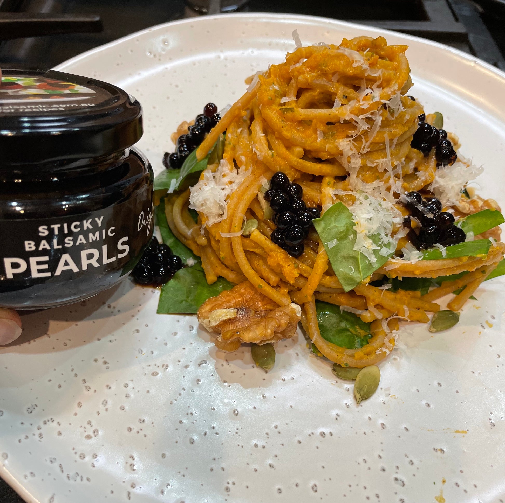 Pasta dish topped with glossy black sticky balsamic pearls, jar at left