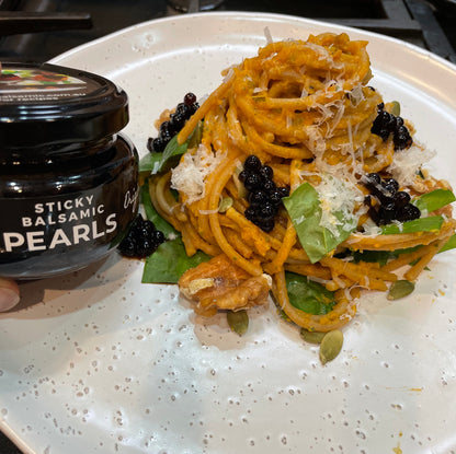 Pasta dish topped with glossy black sticky balsamic pearls, jar at left