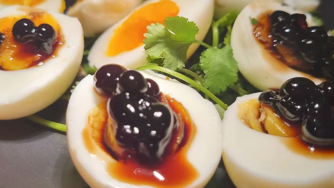 Sticky balsamic pearls on deviled egg halves with orange sauce and black topping