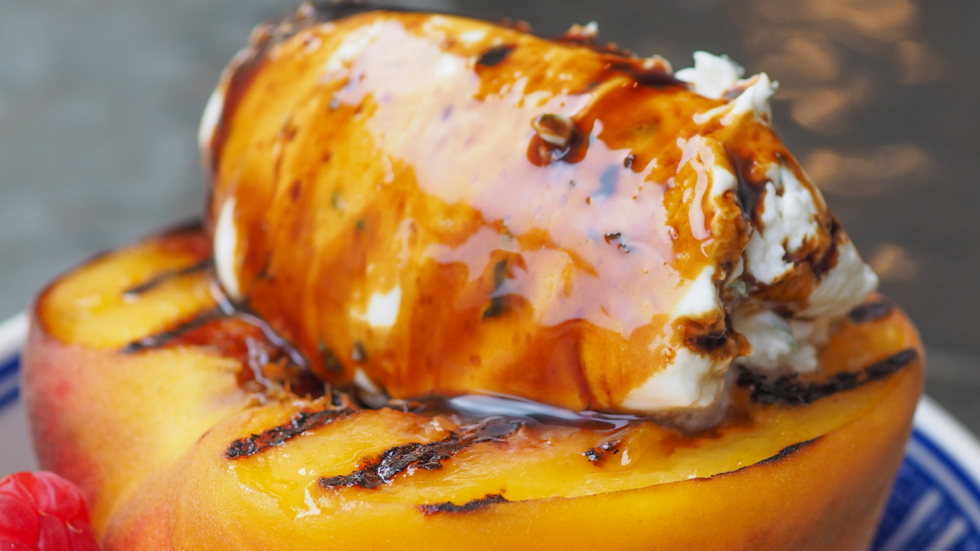 Grilled Peach and Raspberries and Marscapone with Sticky Balsamic drizzled over the top of it. In a patterned blue bowl on a table.