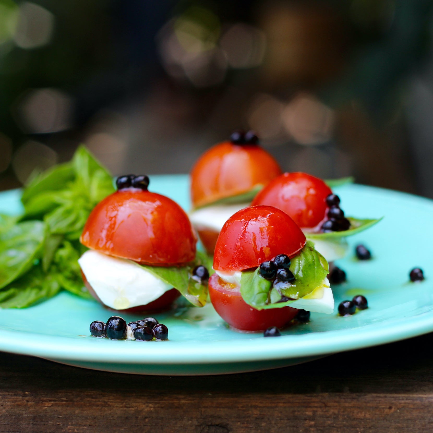Balsamic pearls topping tomato and lettuce on a blue plate