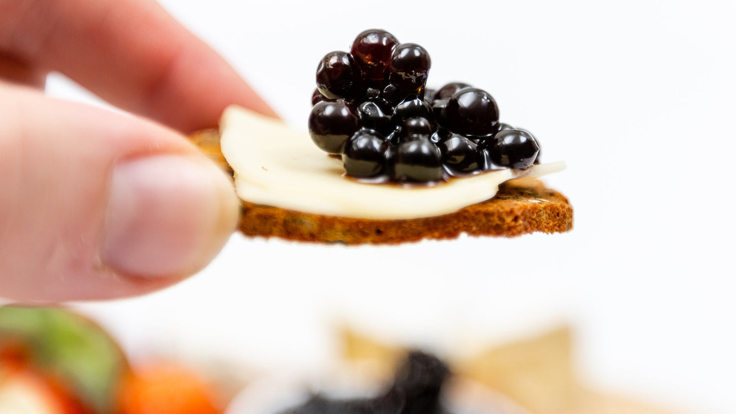 Sticky balsamic pearls on a bread slice held in fingertips