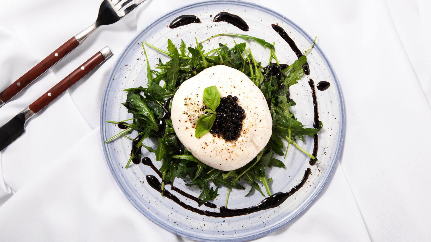 Sticky balsamic pearls on arugula salad with burrata and dark caviar dots
