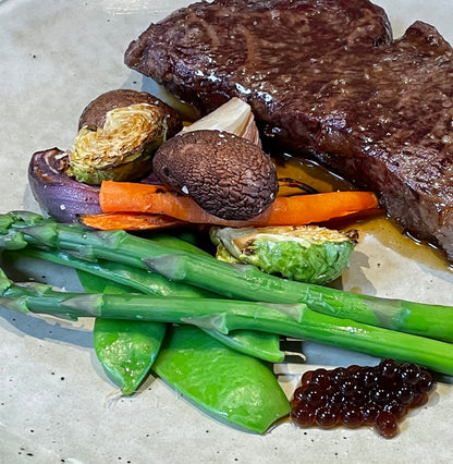 Plated steak with roasted vegetables and dark balsamic pearls garnish