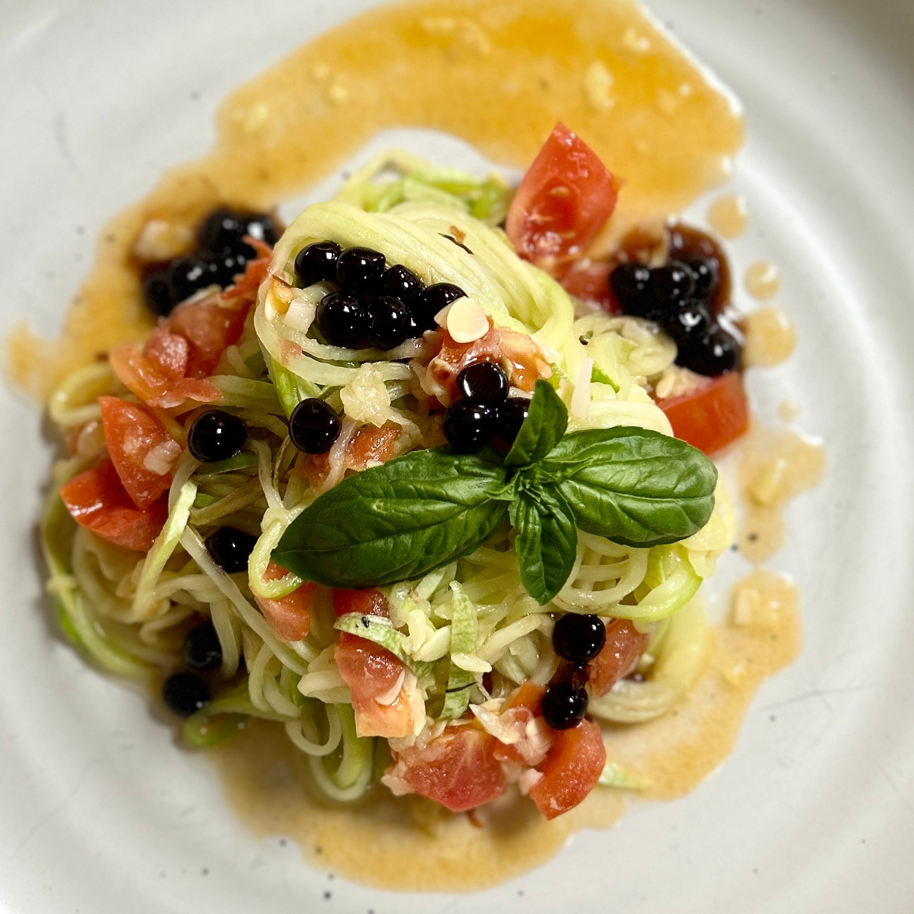 Spaghetti salad plate with tomato, basil, and dark pearls in creamy sauce