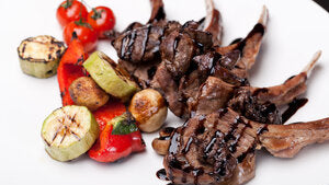 Grilled lamb chops served with assorted grilled vegetables on a white plate.
