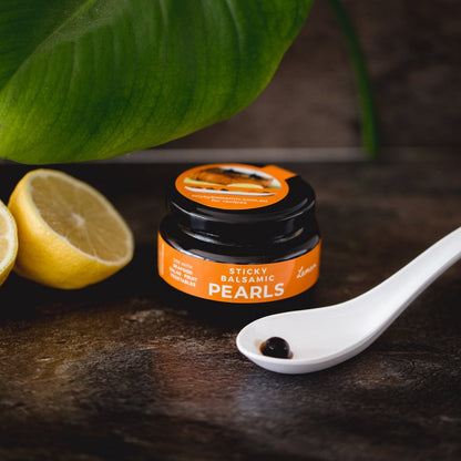 Balsamic pearls jar with spoon of dark pearls and lemon slices
