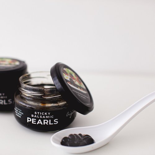 Sticky balsamic pearls jar with open lid and a spoon of glossy black pearls