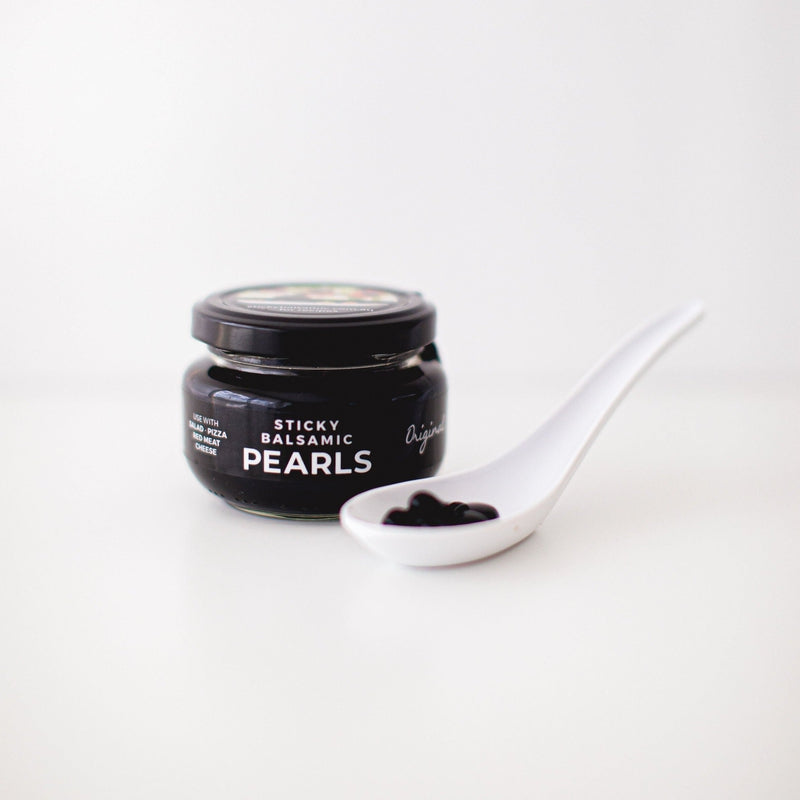 Sticky balsamic pearls jar with white spoon holding glossy black pearls