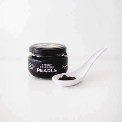 Sticky balsamic pearls jar with white spoon holding glossy black pearls
