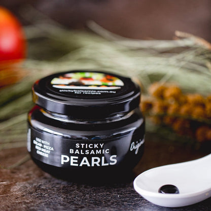 Sticky balsamic pearls jar with spoon of glossy black pearls on a countertop