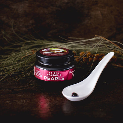 Sticky balsamic pearls jar on a white spoon with dark amber pearls