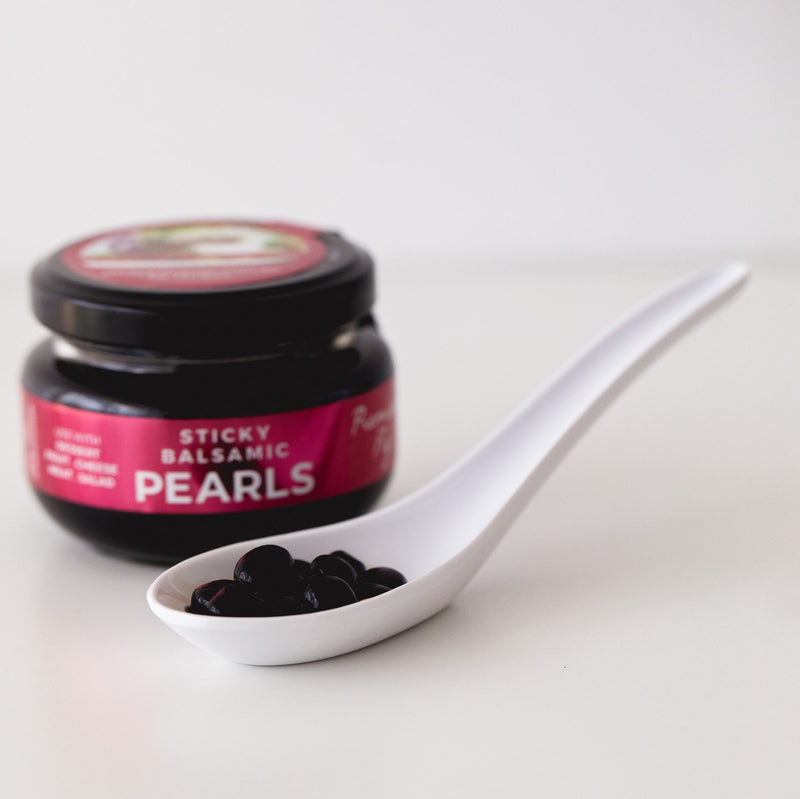 Sticky balsamic pearls spoon with dark pearls beside the jar